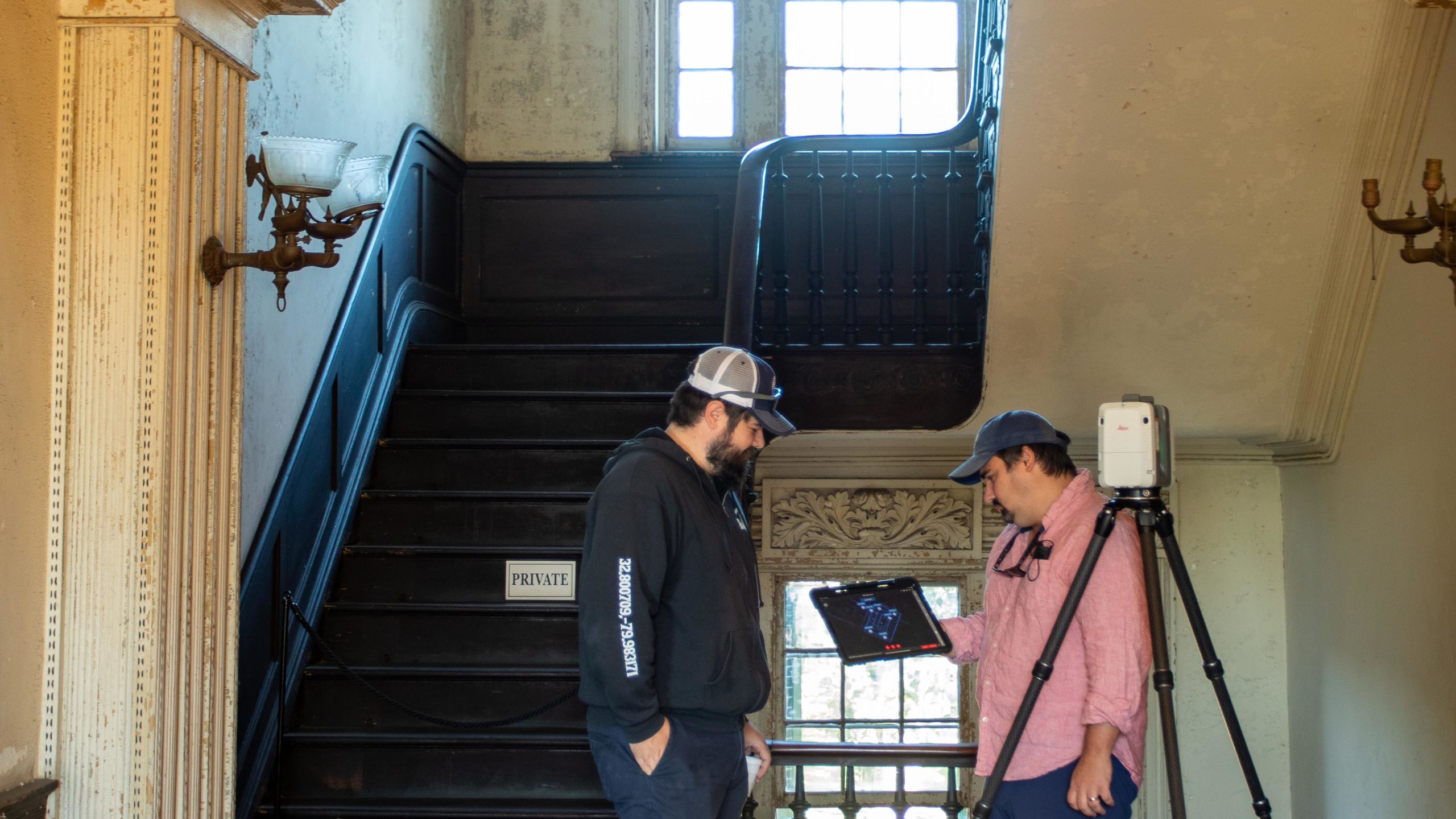 Two staff members standing in the stairwell of the Aiken-Rhett House Museum performing laser scanning
